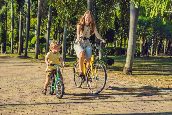 Família feliz está andando de bicicleta ao ar livre e sorrindo. Mãe em uma bicicleta e filho em um balancebike — Fotografia de Stock