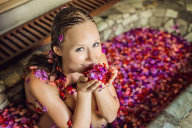 Banyo yaprakları tropikal çiçek ve aroma yağları ile çekici genç kadın. Spa uygulamaları için cilt yenileme. Spa salonu çekici kadın. Lüks spa ve Cilt Bakımı