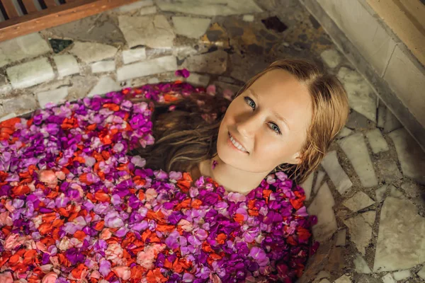 Ελκυστική νεαρή γυναίκα στο μπάνιο με πέταλα τροπικών λουλουδιών και αιθέριων ελαίων. Θεραπείες spa για την αναζωογόνηση δερμάτων. Σαγηνευτική γυναίκα στο κομμωτήριο Spa. Πολυτελή με σπα και φροντίδα δέρματος — Φωτογραφία Αρχείου