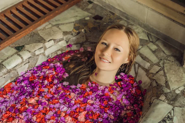 Mulher jovem atraente em banho com pétalas de flores tropicais e óleos de aroma. Tratamentos de spa para rejuvenescimento da pele. Uma mulher sedutora no salão de Spa. Spa de luxo e cuidados com a pele — Fotografia de Stock