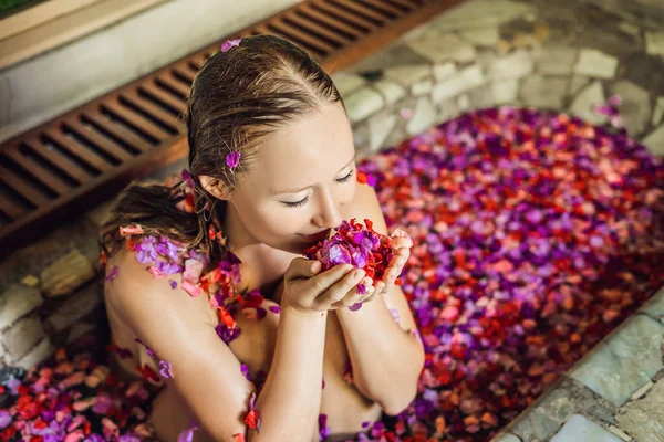 Ελκυστική νεαρή γυναίκα στο μπάνιο με πέταλα τροπικών λουλουδιών και αιθέριων ελαίων. Θεραπείες spa για την αναζωογόνηση δερμάτων. Σαγηνευτική γυναίκα στο κομμωτήριο Spa. Πολυτελή με σπα και φροντίδα δέρματος — Φωτογραφία Αρχείου