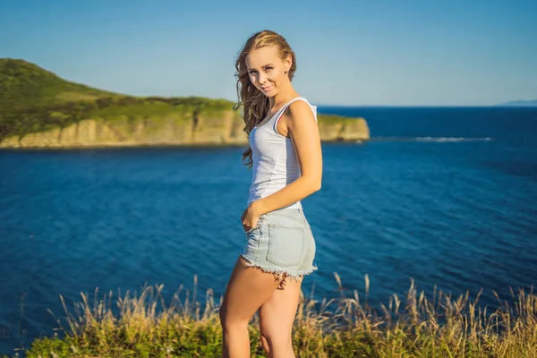 Young woman in jeans shorts posing against the blue sea. Wearing jeans stylish shorts and striped shirt — Stock Photo, Image
