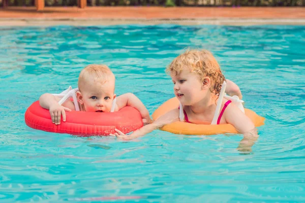 Irmão e irmã se divertindo na piscina em círculos infláveis — Fotografia de Stock