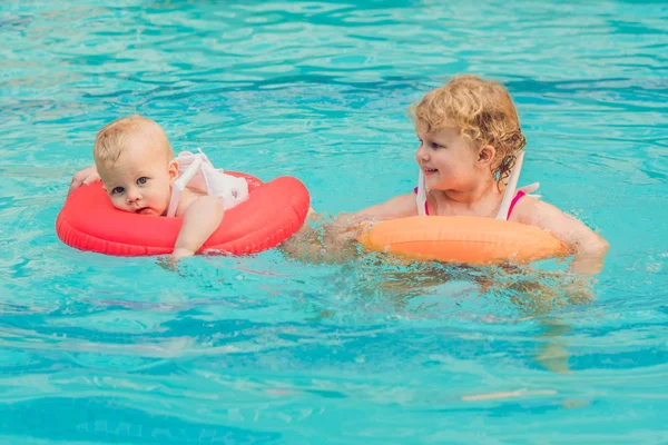 Irmão e irmã se divertindo na piscina em círculos infláveis — Fotografia de Stock