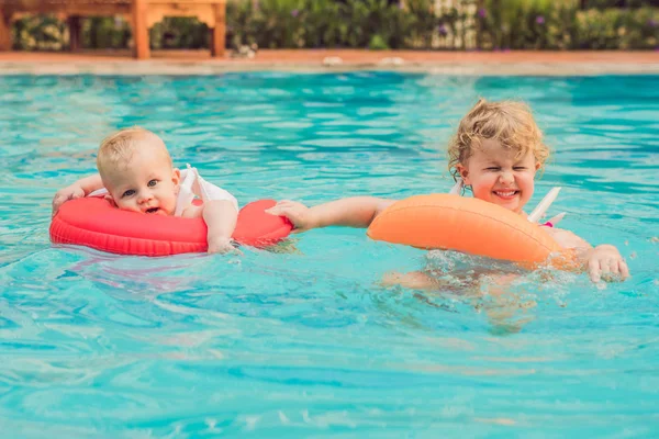 Irmão e irmã se divertindo na piscina em círculos infláveis — Fotografia de Stock