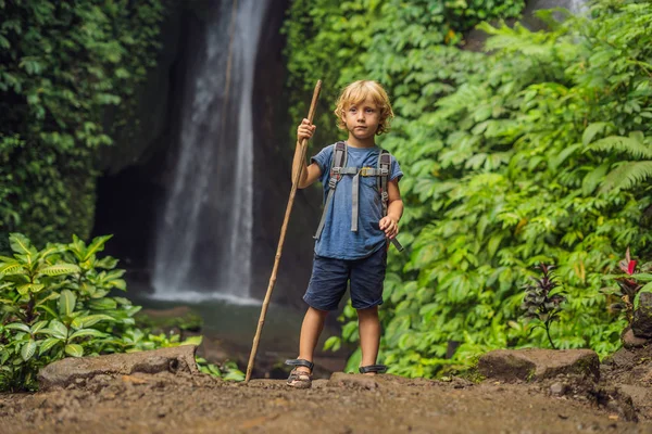 Niño con un bastón de trekking en el fondo de la cascada Leke Leke en la isla de Bali Indonesia. Viajar con concepto de niños —  Fotos de Stock