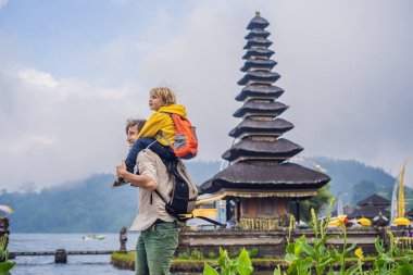 Dad and son in the background of Pura Ulun Danu Bratan, Bali. Hindu temple surrounded by flowers on Bratan lake, Bali. Major Shivaite water temple in Bali, Indonesia. Hindu temple. Traveling with clipart