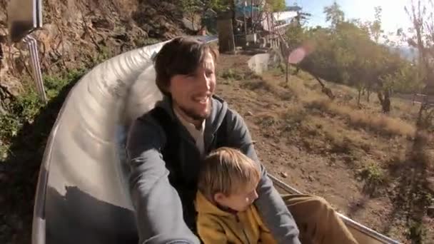 Strzał slowmotion ojca i syna, jazda w dół na alpejskim roller coaster w lesie jesienią — Wideo stockowe