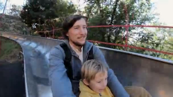 Fotografía en cámara lenta de un padre y un hijo cabalgando por la montaña rusa alpina en un bosque de otoño — Vídeos de Stock