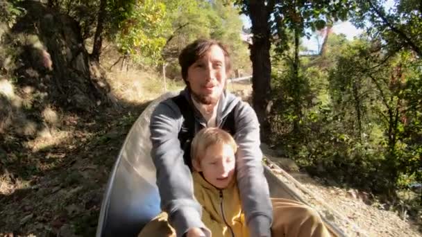 Fotografía en cámara lenta de un padre y un hijo cabalgando por la montaña rusa alpina en un bosque de otoño — Vídeos de Stock