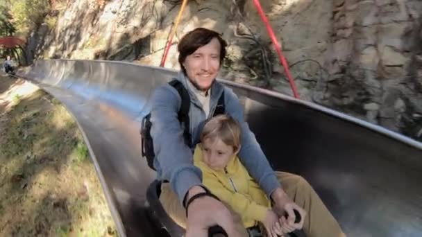 Fotografía en cámara lenta de un padre y un hijo cabalgando por la montaña rusa alpina en un bosque de otoño — Vídeo de stock