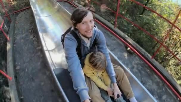 Fotografía en cámara lenta de un padre y un hijo cabalgando por la montaña rusa alpina en un bosque de otoño — Vídeos de Stock