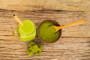 Ahşap arka plan matcha yeşil çay sütlü buz mason kavanoza, matcha tozu ve şeker ile yapılmış. Ev yapımı Matcha Latte çayları ile süt sıfır atık