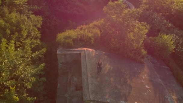 Foto aérea de una joven mujer corriendo en el territorio de una antigua fortaleza de la Primera Guerra Mundial al atardecer, al amanecer. Lente destellos del sol poniente . — Vídeos de Stock