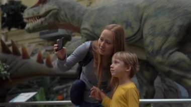 Beijing, Çin - 22 Ekim 2018: Genç bir kadın ve onun küçük oğlu turistler dinozorlar bir Tyrannosaur'u hareketli bir model ile bir arka plan hareketli bir resim çekmek