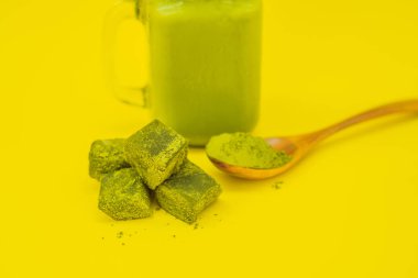 Mason kavanoza ve saman buzlu yeşil çay kahve ve kaşık toz matcha ve şeker ile matcha sarı zemin üzerine yapılmış. Ev yapımı Matcha Latte çayları ile süt sıfır atık