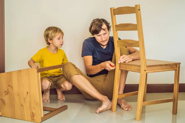 Far och son monterar ihop möbler. Pojken hjälper sin pappa hemma. Glad familj koncept — Stockfoto