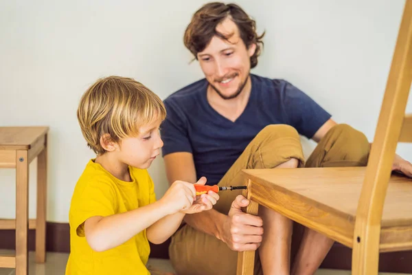 Far och son monterar ihop möbler. Pojken hjälper sin pappa hemma. Glad familj koncept — Stockfoto