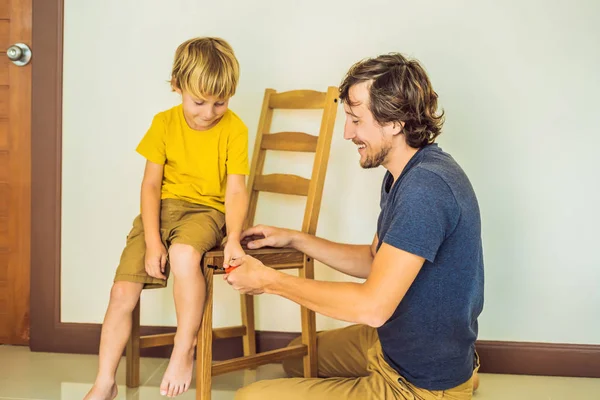 Far och son monterar ihop möbler. Pojken hjälper sin pappa hemma. Glad familj koncept — Stockfoto