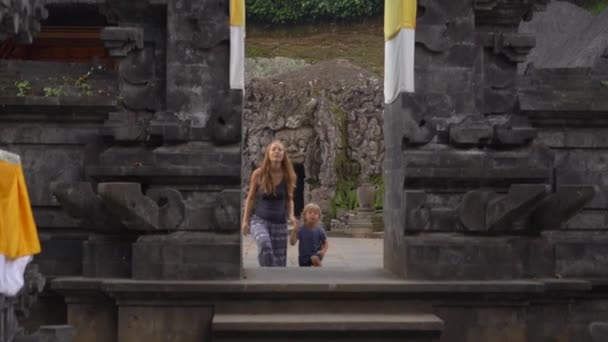 Fotografía en cámara lenta de una mujer joven y su pequeño hijo visitando la cueva del elefante, Goa Gajah en el pueblo de Ubud en la isla de Bali — Vídeos de Stock