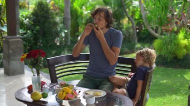 Genç bir baba ve küçük oğlu bir avokado tost ve çok meyve bahçesi ile çevrili kendi terasta kahvaltı Slowmotion atış