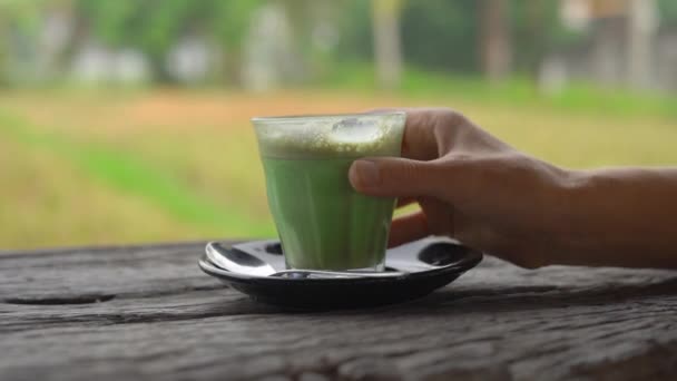 一个年轻女子在热带咖啡馆里喝绿茶抹茶拿铁的慢镜头, 可以看到稻田的景色 — 图库视频影像