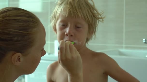 Jovem mulher escovando os dentes para seu filho em um banheiro — Vídeo de Stock