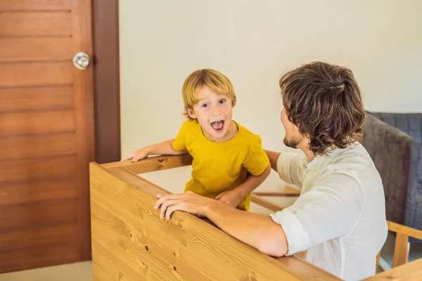 Far och son monterar ihop möbler. Pojken hjälper sin pappa hemma. Glad familj koncept — Stockfoto