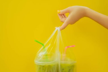 İki yeşil çay sütlü buzun içinde plastik kap ve saman sarı zemin üzerine sarı manikür ile kadın elinde. Ev yapımı buzlu Matcha Latte sütlü çay götürün