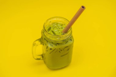 Buz mason kavanoza ve saman sarı zemin üzerine yeşil çay kahve. Ev yapımı Matcha Latte çayları ile süt sıfır atık