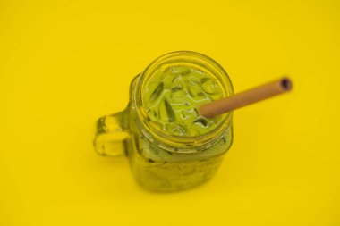 Buz mason kavanoza ve saman sarı zemin üzerine yeşil çay kahve. Ev yapımı Matcha Latte çayları ile süt sıfır atık