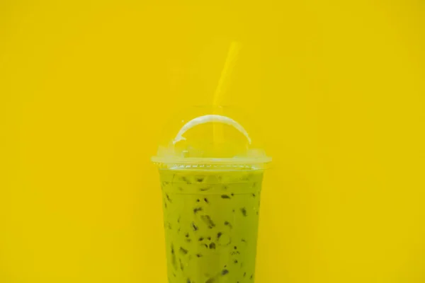 Caffè al tè verde con ghiaccio in tazza di plastica e paglia in mano femminile con manicure gialla su sfondo giallo. Fatto in casa tè Latte Matcha ghiacciato con latte da asporto — Foto Stock