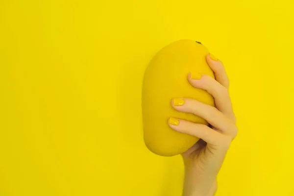 Рука с желтым маникюром с желтым спелым манго на желтом фоне — стоковое фото