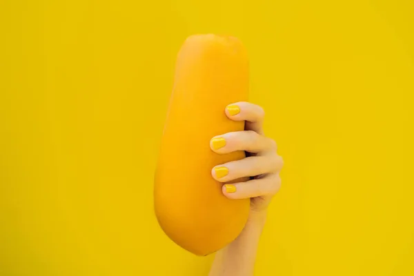 Рука с желтым маникюром, держащая апельсиновую спелую папайю на желтом фоне — стоковое фото