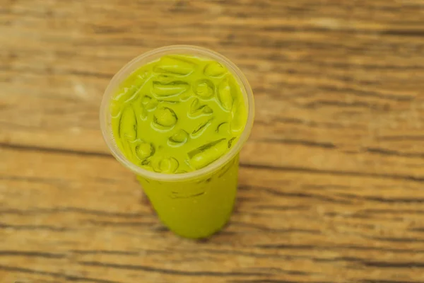 Grüntee-Latte mit Eis in Plastikbecher und Stroh auf Holzgrund. hausgemachter Eistee Matcha Latte Tea mit Milch zum Mitnehmen — Stockfoto