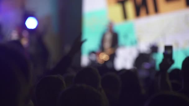 Plan au ralenti de silhouettes de personnes dans une foule sur le fond de la scène lors d'un concert — Video