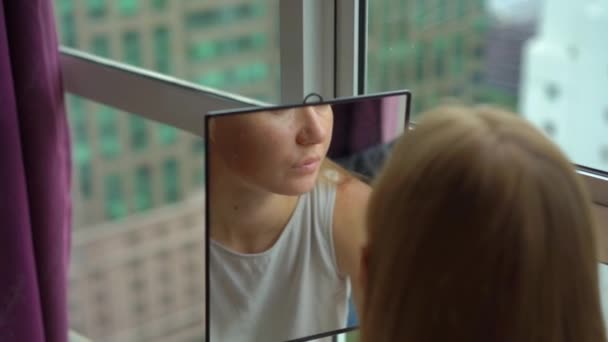 Super Slow Motion shot van een jonge vrouw doen haar make-up sittng door een panoramisch venster in het centrum van een stad met wolkenkrabbers op een achtergrond — Stockvideo