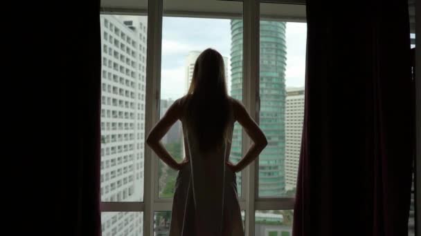Superslowmotion は、パノラマの景色と彼女のダウンタウンのアパートの窓のそばに立って成功した豊富な若い女性のショット。成功のコンセプトです。彼女のダウンタウンのアパートで満たされた人生のコンセプト。成功 — ストック動画