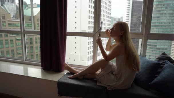 超级慢动作拍摄一个年轻女子在一个有摩天大楼背景的城市的市中心的全景窗口旁化妆 — 图库视频影像