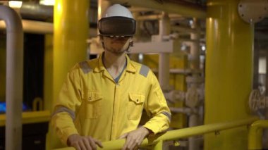 Endüstriyel ortamda sarı iş üniformalı genç adam petrol platformu veya sıvılaştırılmış gaz tesisi kullanan Vr gözlük. Slowmotion atış