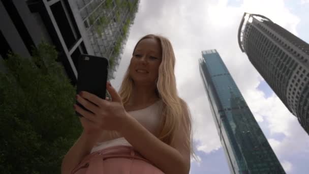 Superslowmotion plan d'une jeune femme thar utiliser un smartphone dans le centre-ville avec des gratte-ciel à l'arrière-plan. Navigation à travers le concept de la ville. Concept de transport public. Concept de réservation de taxi — Video