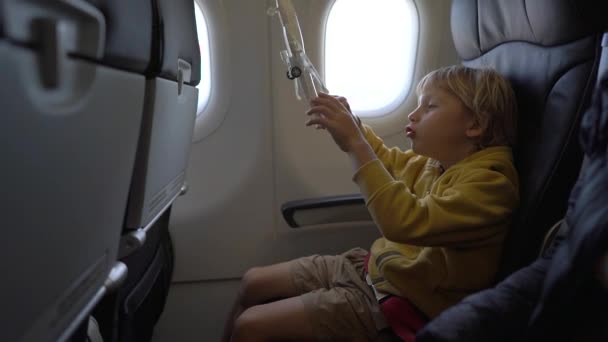 Повільний постріл маленького хлопчика, який грає з білим іграшковим літаком, сидить у кріслі на борту літака. Концепція свободи. Концепція дитинства. Концепція подорожей дітей — стокове відео