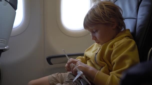 Filmagem em câmera lenta de um menino que brinca com um avião de brinquedo branco sentado em uma cadeira a bordo de um avião. Conceito de liberdade. Conceito de infância. Conceito de viagem infantil — Vídeo de Stock