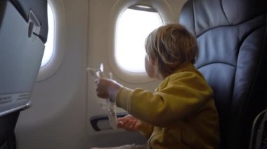 Bir sandalyede bir uçağın onboard oturan beyaz oyuncak uçak ile oynayan küçük bir çocuk Slowmotion vurdu. Özgürlük kavramı. Çocukluk kavramı. Çocuklar seyahat kavramı