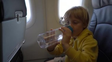 Slowmotion atış bir sandalyede bir uçağın uçakta oturuyor yeniden kullanılabilir plastik şişe suyu içer küçük bir çocuk. Çocuk kavramı seyahat. Tarafından plastik kavramı kirliliği azaltmak. Yeniden kullanılabilir