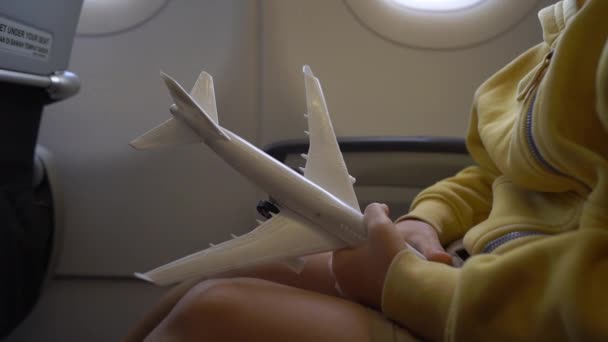 Slowmotion shot of a little boy that plays with white toy airplane sitting in a chair onboard of an airplane. Freedom concept. Childhood concept. Children travel concept — Stock Video