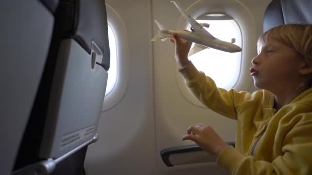 Slowmotion 흰색 장난감 비행기는 비행기의 기내의 자에 앉아 함께 재생 하는 어린 소년의 총. 자유 개념입니다. 어린 시절 개념입니다. 어린이 여행 컨셉 — 비디오