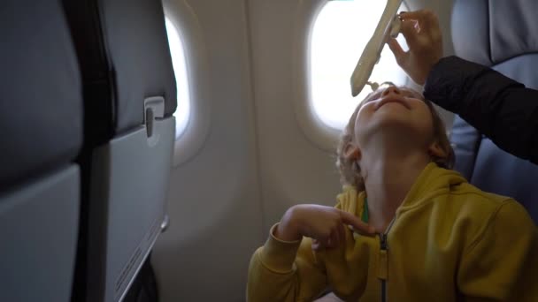 Fotografía en cámara lenta de un niño que juega con un avión de juguete blanco sentado en una silla a bordo de un avión. Concepto de libertad. Concepto de infancia. Concepto de viaje infantil — Vídeos de Stock