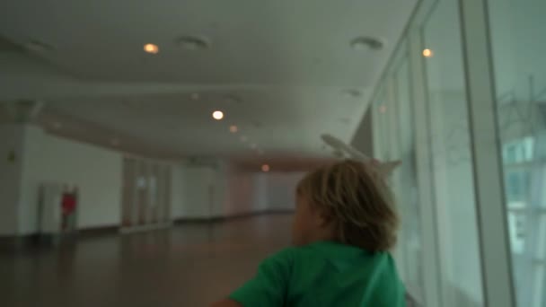 Slowmotion shot of a little boy that run through airport holding white toy airplane in his hand. Freedom concept. Childhood concept. Children travel concept — Stock Video