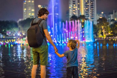 Baba ve oğul turist gece, göl kenarında renkli Çeşme arka plan üzerinde yakınındaki İkiz Kuleler'in tarafından şehir üzerinde arka plan ile. Kuala Lumpur, Malezya